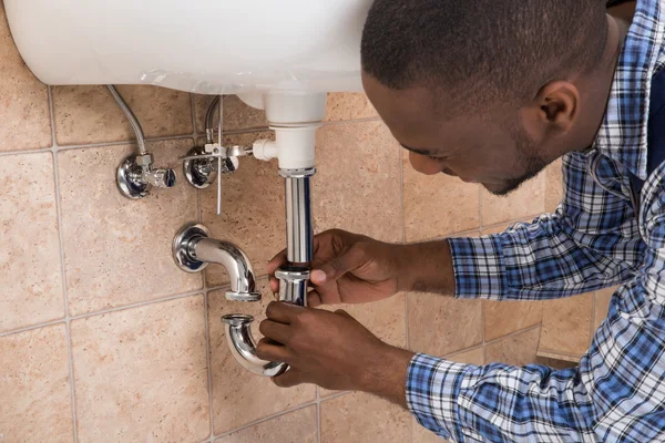 Plumber fitting the chrome trap and pipework under a hand basin